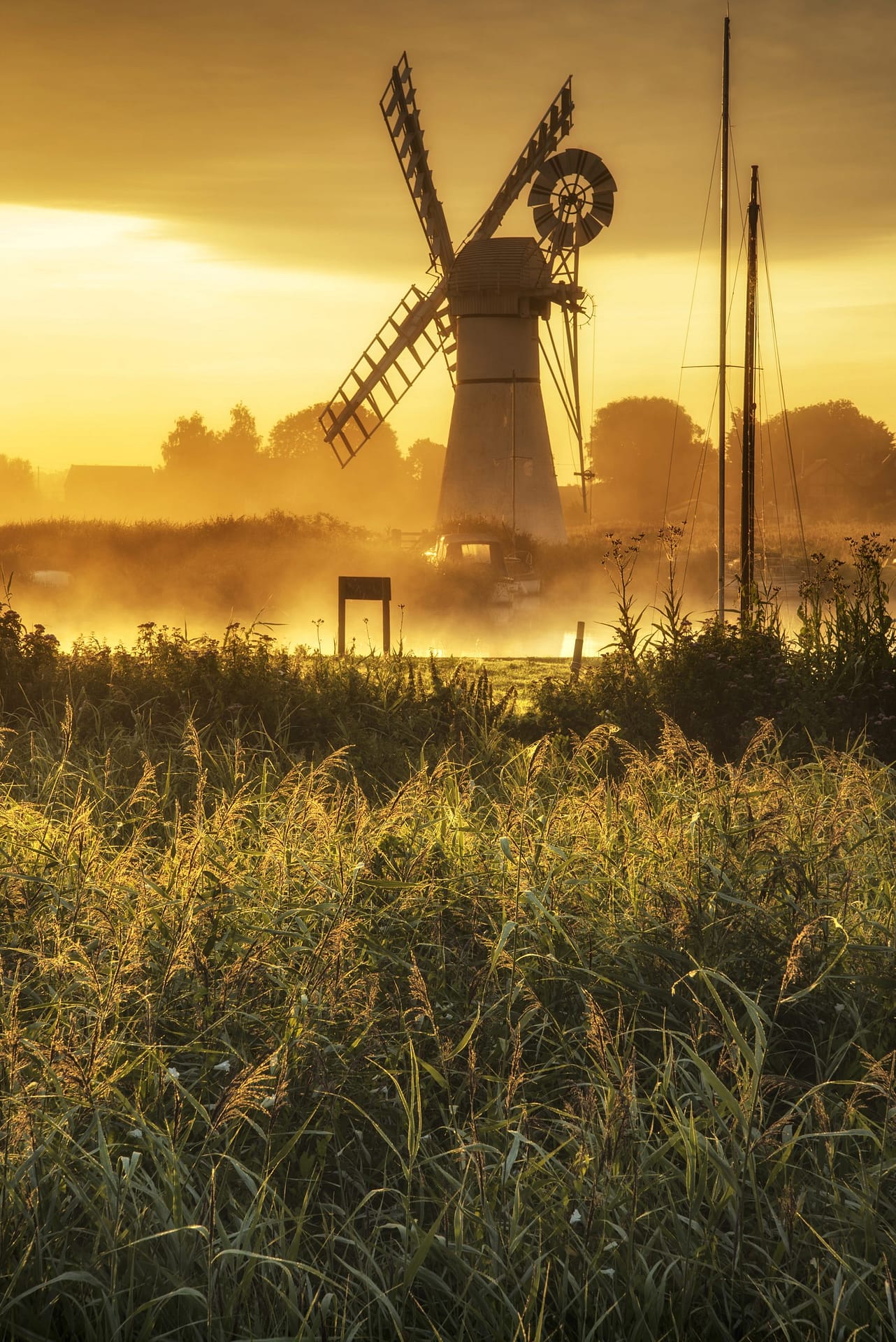 A water-pump windmill on the Norfolk Broad, UK, set against a misty background.